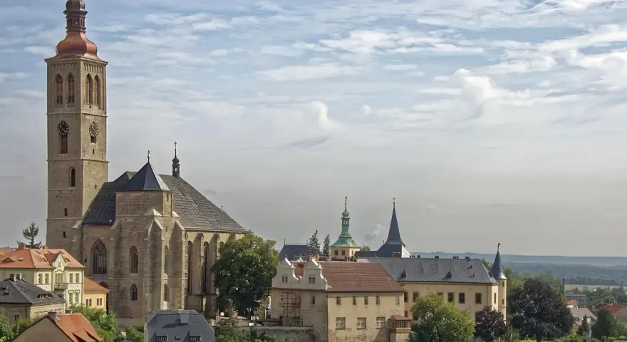 Majestatyczna katedra i zabytkowe budynki w Kutnej Horze pod błękitnym, chmurnym niebem.