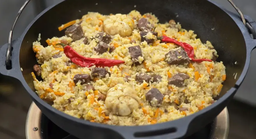 Herzhaftes Plov-Rezept im Kessel: Reis, Fleisch, Karotten, Knoblauch und scharfe Chilis. Ein Festmahl!