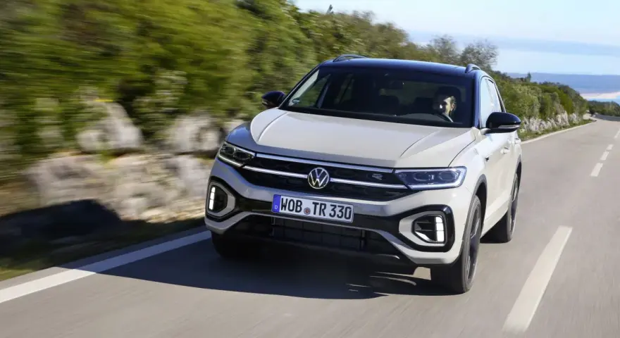 Jasnoszary Volkswagen T-Roc jedzie po krętej drodze. Nawet przy potencjalnych usterkach, ten model prezentuje się dynamicznie.