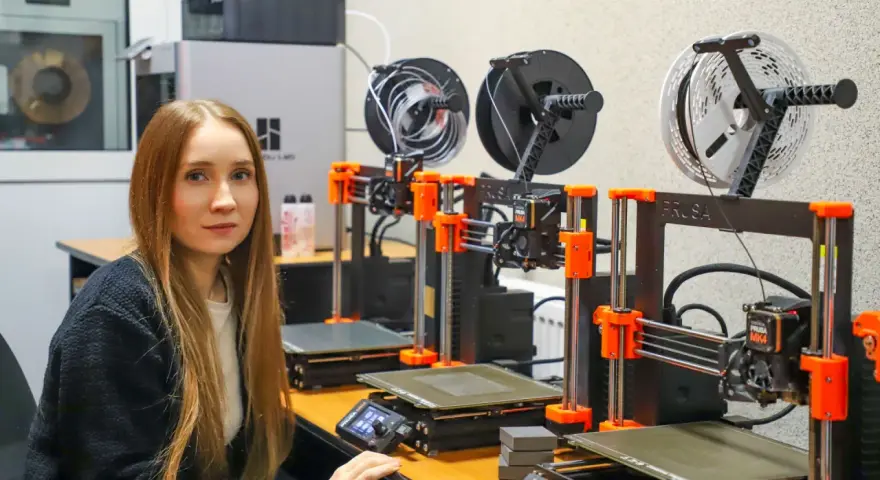 Kobieta w laboratorium obok rzędu drukarek 3D, które są kluczowe dla historii drukarki 3d.
