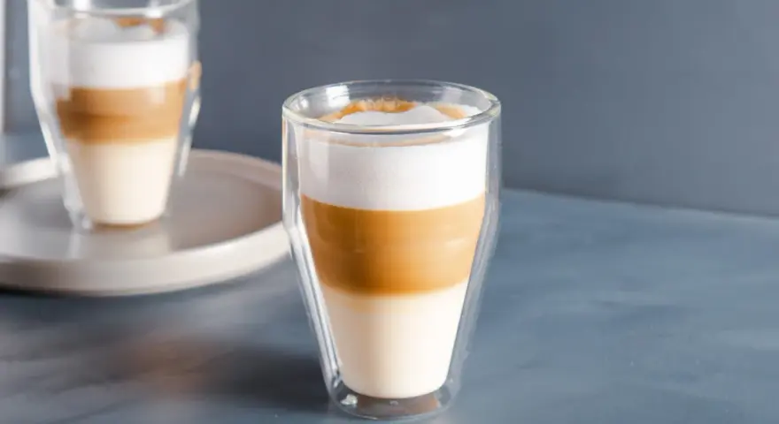 Dwa latte macchiato w szklankach z podwójnymi ściankami, z wyraźnie widocznymi warstwami mleka i kawy.