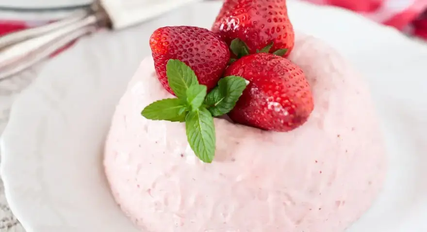 Deliziosa bavarese alle fragole, guarnita con fragole fresche e menta, su un piatto bianco.