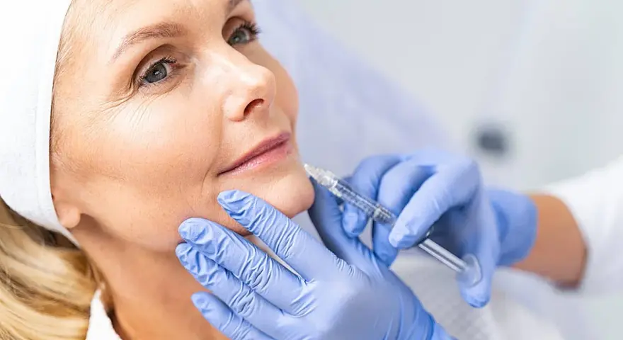 Mujer recibe tratamiento facial con exosomas. Manos enguantadas aplican inyección para rejuvenecer la piel.