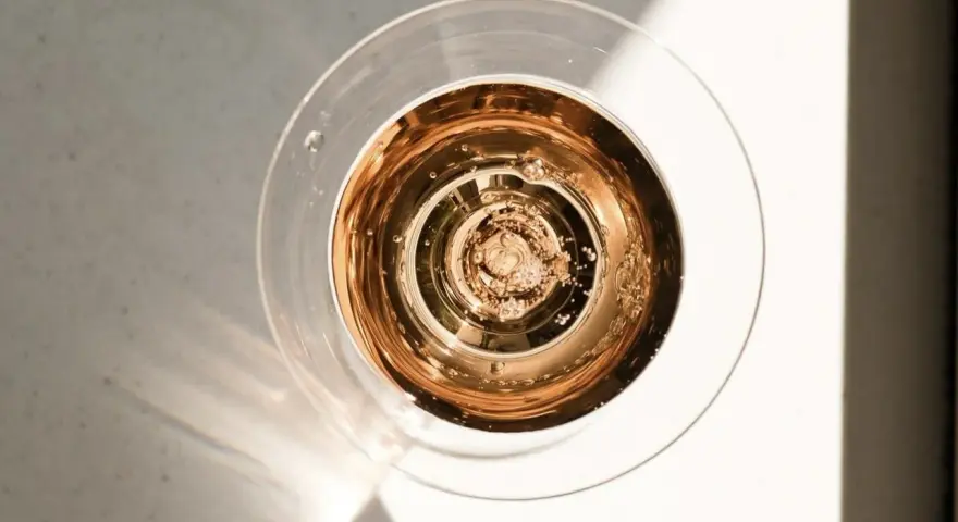 Szklanka z różowym, musującym winem, które wygląda jak tanie wino, ale jest podane w elegancki sposób. Bąbelki unoszą się ku górze.