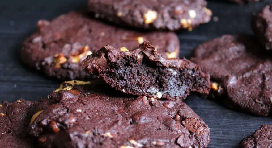 Schokoladenkekse mit Nüssen, die an das subway cookies rezept erinnern. Ein Keks ist zerbrochen und zeigt die saftige Innenseite.