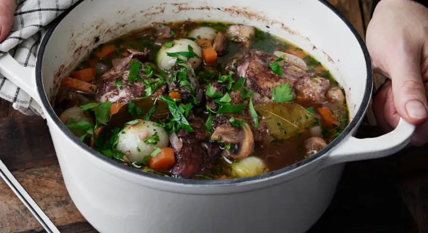 En gryta med mustig coq au vin, fylld med möra kycklingbitar, champinjoner, lök och morötter, toppad med färsk persilja.