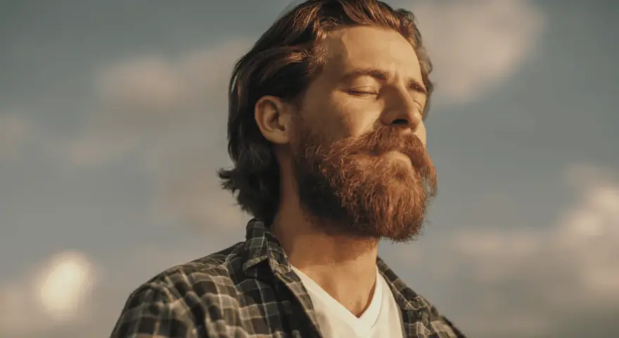 Homme à la barbe rousse, yeux fermés, profitant du soleil. Une image qui évoque le bien-être et la vitalité, peut-être liée à un test libido homme.