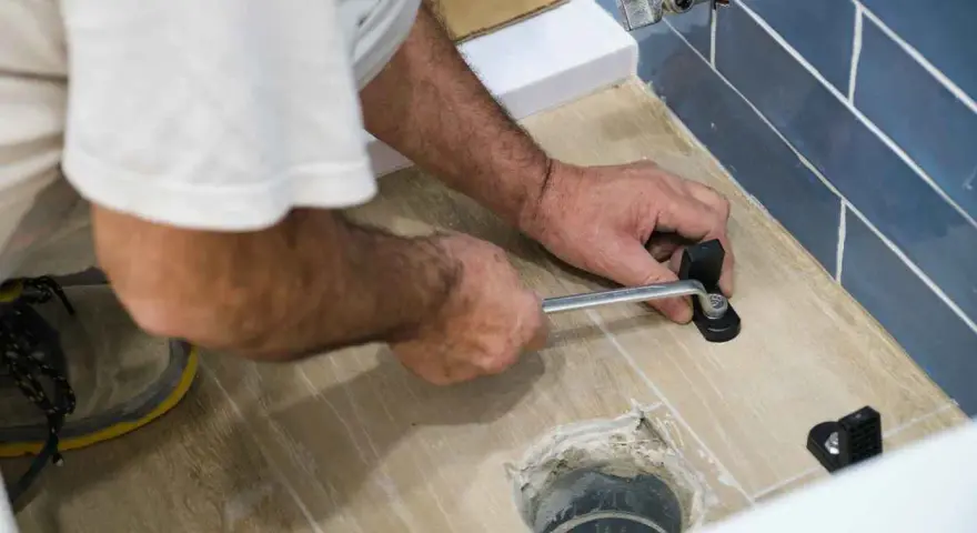 A person uses a wrench to tighten a toilet flange bolt, demonstrating how to replace a toilet flange.