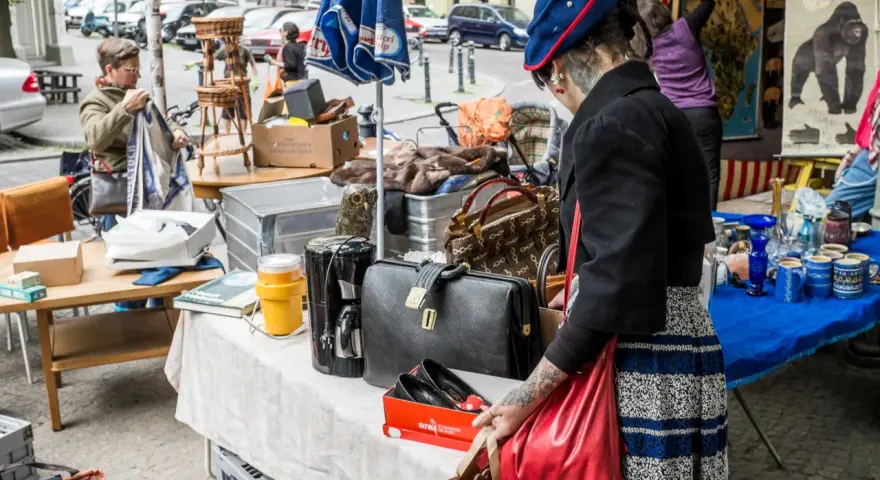 Frau mit Tätowierungen auf dem Arm sucht auf einem antik flohmarkt nach Schätzen. Sie hält eine rote Tasche.