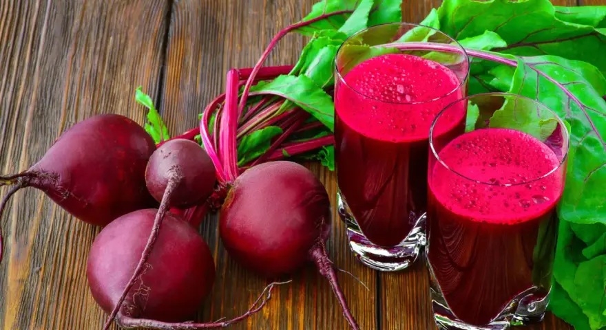 Frische rote Bete und zwei Gläser mit leuchtend rotem Rote-Bete-Saft stehen auf einem Holztisch.