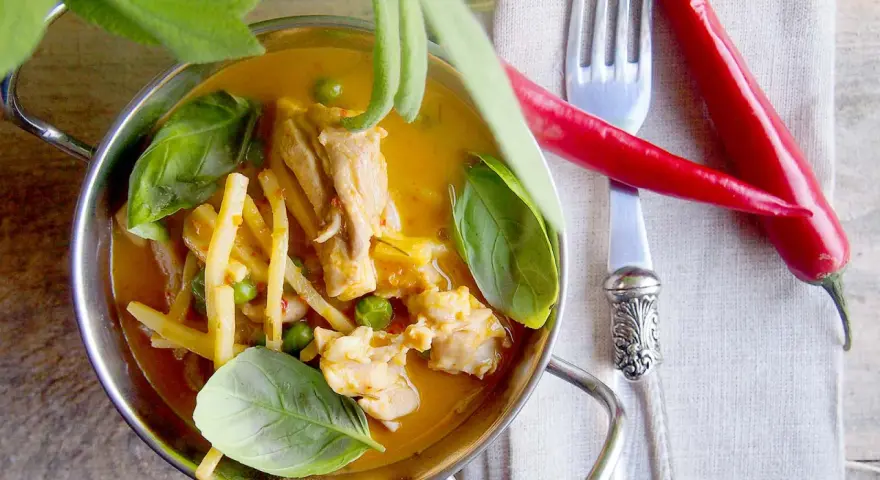 Aromatyczne czerwone curry z kurczakiem, bambusem i groszkiem, ozdobione świeżą bazylią i papryczkami chili.