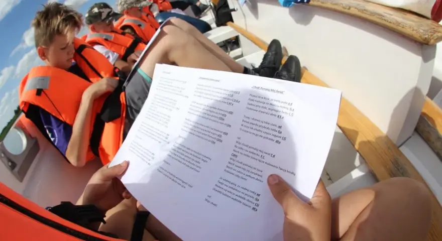 Dzieci na łodzi z kamizelkami ratunkowymi śpiewają piosenki żeglarskie dla dzieci.