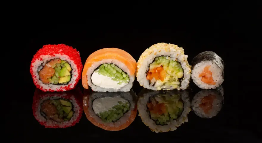 Różne rodzaje sushi: rolka z łososiem i awokado w ikrze, z łososiem i serkiem, z sezamem i warzywami, oraz klasyczne maki z łososiem.