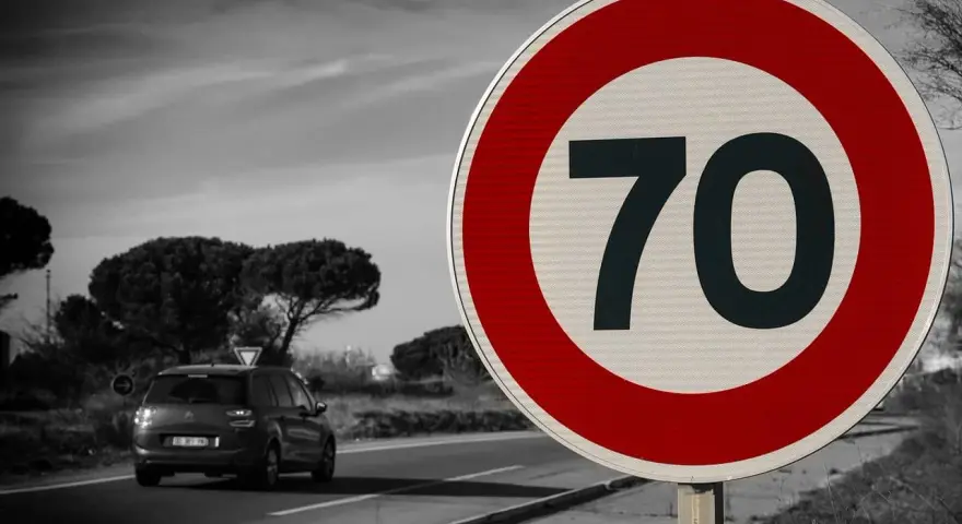 Segnale 226: limite di velocità 70. Un'auto viaggia su una strada panoramica.