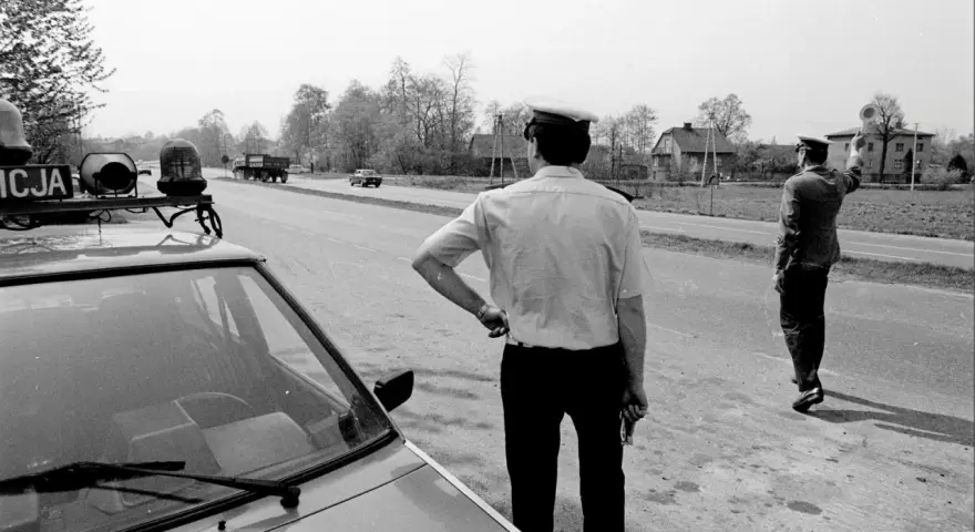 Policjanci na gierkówce kontrolują ruch. Jeden z nich stoi przy radiowozie, drugi kieruje ruchem.