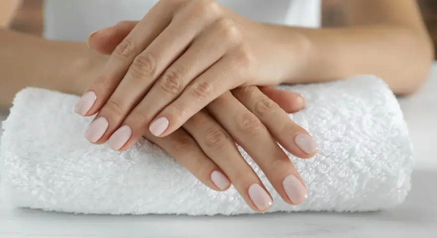 Dłonie z idealnym, jasnoróżowym manicurem kombinowanym spoczywają na białym ręczniku.