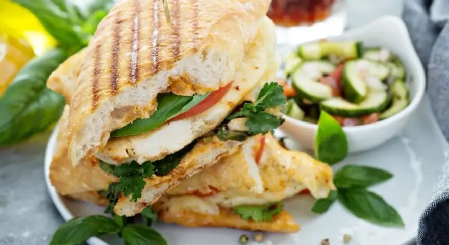 Pyszne panini z kurczakiem, pomidorem i bazylią, podane z sałatką z ogórka. Idealne na lekki posiłek.