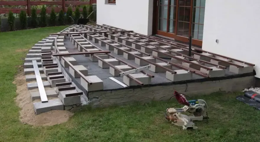 Budowa tarasu z deski kompozytowej w toku. Widać konstrukcję nośną z bloczków betonowych i legarów, gotową do ułożenia desek.
