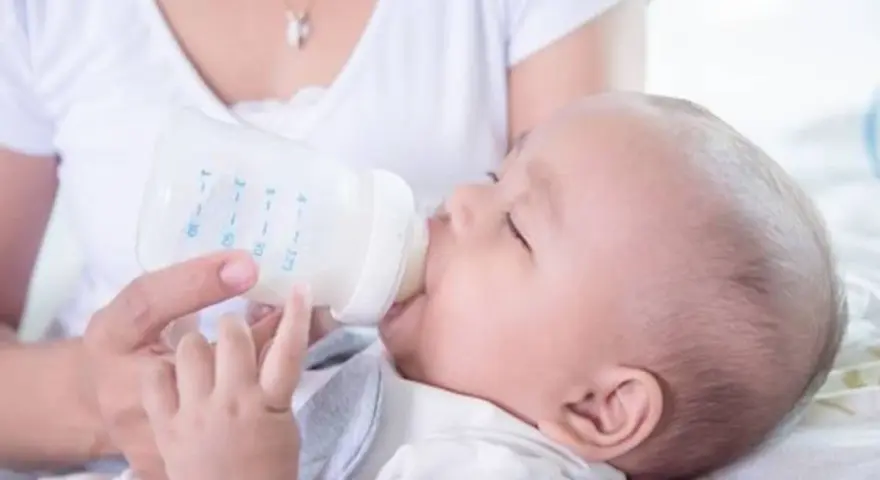 Dziecko pije mleko modyfikowane z butelki. Mama karmi maluszka.