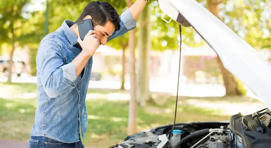 Mann telefoniert neben offenem Motorraum. Was ist beim Abschleppen zu beachten bei PKW Defekt?