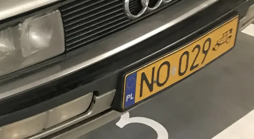 Zbliżenie na przednią część samochodu z żółtą tablicą rejestracyjną "NO 029" i logo Audi.