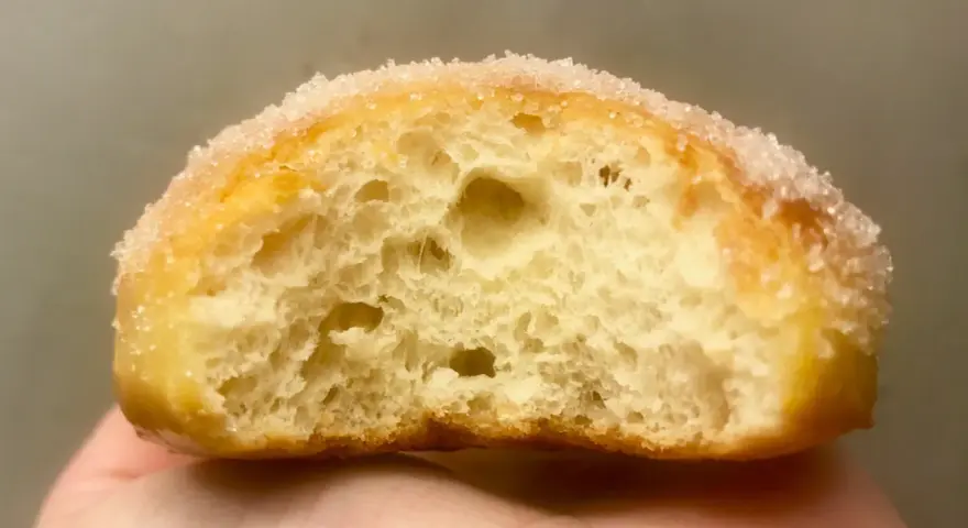 Gros plan d'un beignet sucré, sa mie aérée parfaite pour une recette beignet maison.