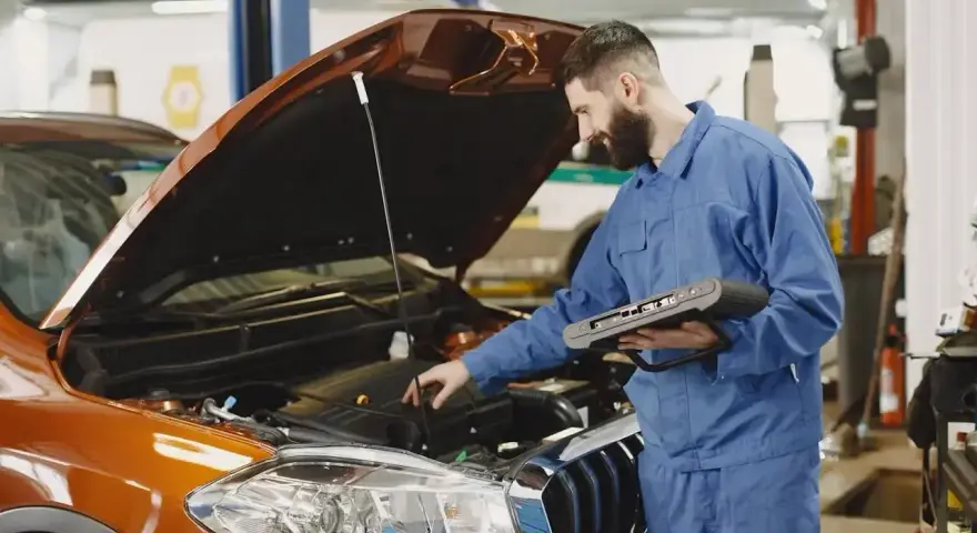 Mechanik z komputerem diagnostycznym sprawdza silnik pomarańczowego auta. Zastanawiasz się, ile trwa wymiana oleju?