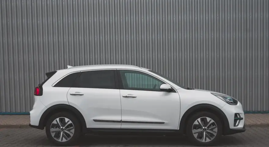 Biały Kia Niro EV widziany z boku na tle szarej, falistej ściany.