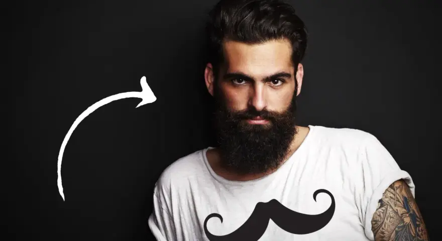 Hombre con barba tupida, quizás decidiendo dejarse barba por primera vez. Camiseta blanca con estampado de bigote.
