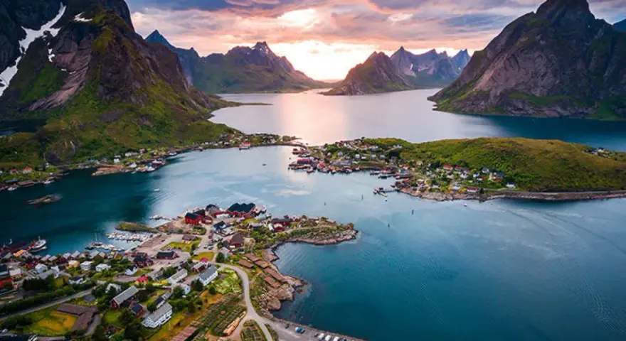 En pittoresk by med röda hus vid en fjord, omgiven av dramatiska berg. En av de fina platserna i Norge, badande i solnedgångens ljus.
