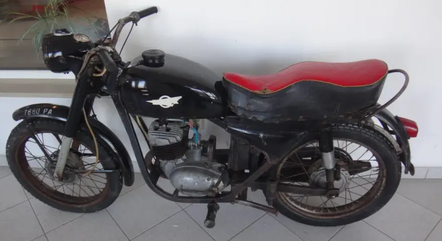 Czarny motocykl wsk 125 z czerwoną kanapą, stojący na szarej podłodze.