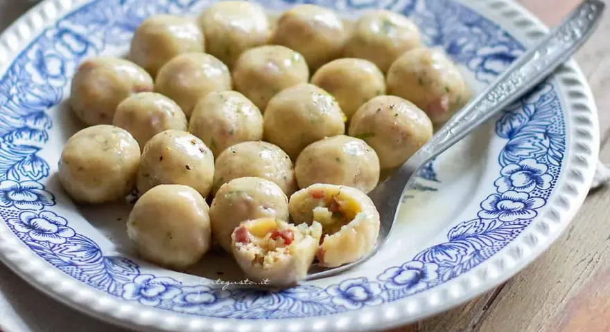 Gnocchi di pane saporiti, serviti su un piatto decorato. Uno è tagliato a metà, rivelando un ripieno gustoso.