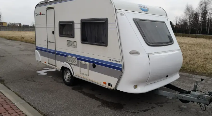 Biała przyczepa kempingowa Hobby 400 de luxe easy z niebieskimi pasami, gotowa na wakacyjne podróże.