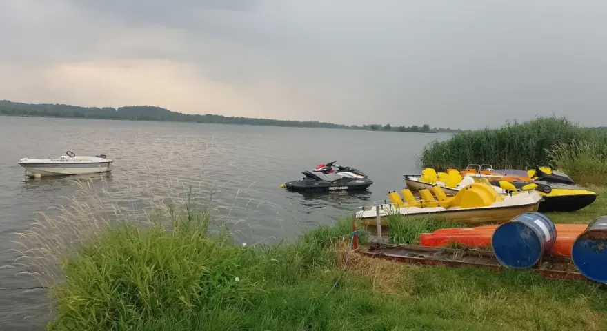 Na jeziorze Paczkowskim pływa motorówka i skutery wodne. Na brzegu czekają rowery wodne i kajaki.