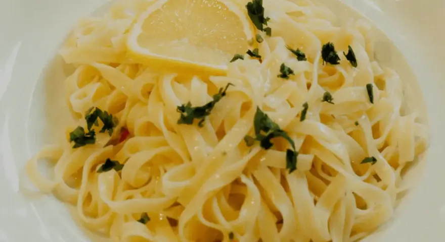En portion krämig citronpasta med färsk persilja och en citronskiva. Perfekt till ett glas vitt vin.
