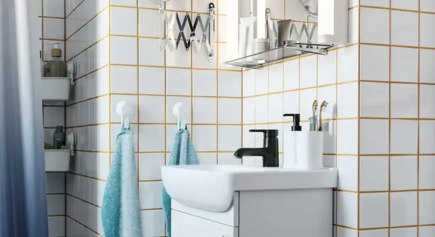 Salle de bain moderne avec carrelage blanc et joints dorés, évier, robinetterie noire et accessoires. Idéal pour un plancher chauffant avec un joint de 2mm.
