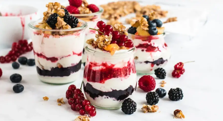 Leckeres Dessert mit Beeren und Joghurt in Gläsern geschichtet, garniert mit Granola und frischen Früchten.