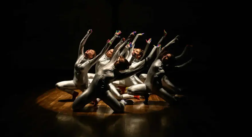 Un groupe de danseurs en costumes argentés, mains levées, dans un photo spectacle captivant.