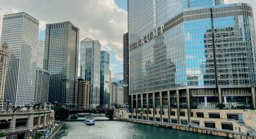 Chicago's iconic skyline along the river, with the Trump Tower reflecting the clouds. A boat glides by, making you wonder, is Chicago worth visiting?