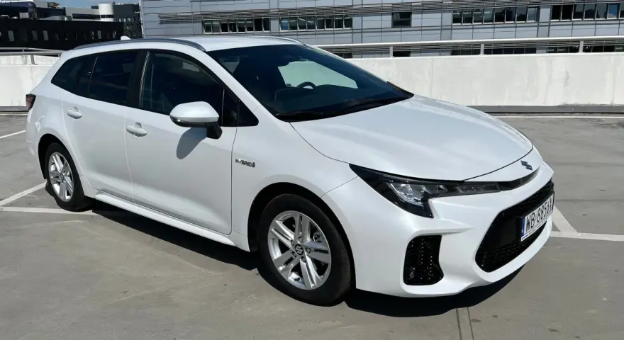 Biały Suzuki Swace Hybrid na parkingu. Elegancki kombi z nowoczesnym designem, gotowy na każdą podróż.