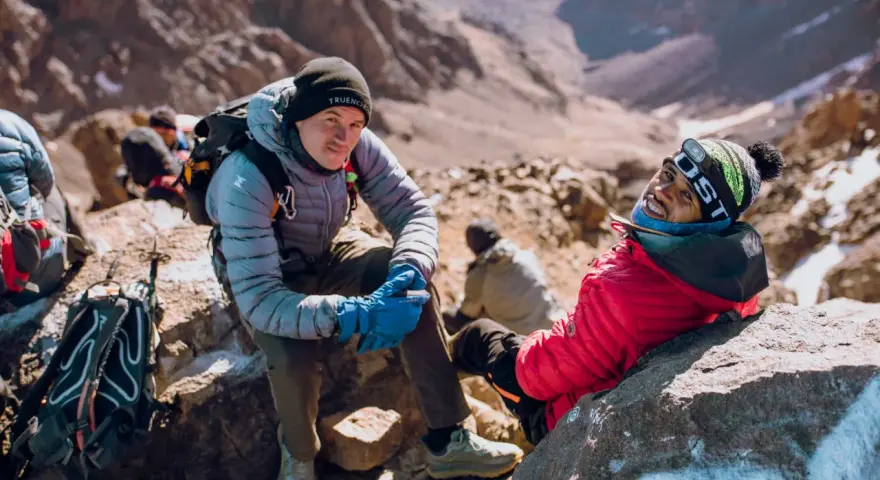 Uśmiechnięci alpiniści podczas wyprawy na Toubkal. W tle skaliste zbocza górskie.