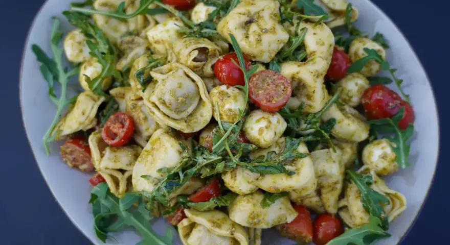 Ein köstlicher Tortellini-Salat mit Pesto, Kirschtomaten und Mozzarella-Kugeln, garniert mit Rucola.