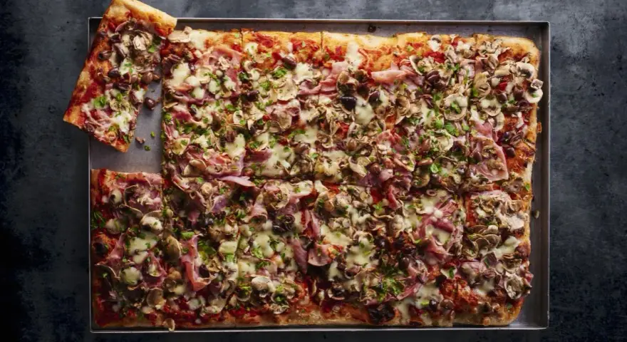 Pyszna pizza domowa przepis na blachę z szynką, pieczarkami i oliwkami. Idealna na rodzinne spotkanie.