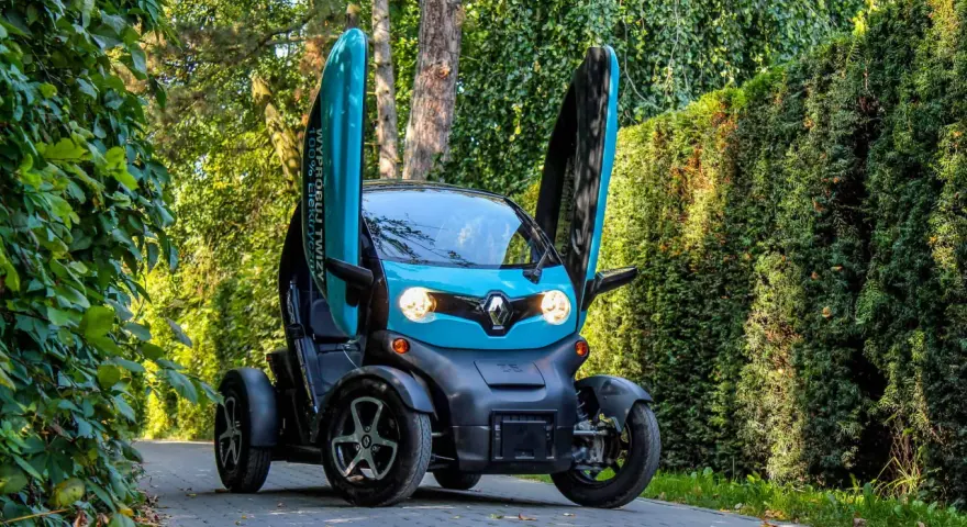 Niebieski Renault Twizy z otwartymi drzwiami stoi na ścieżce wśród zieleni.