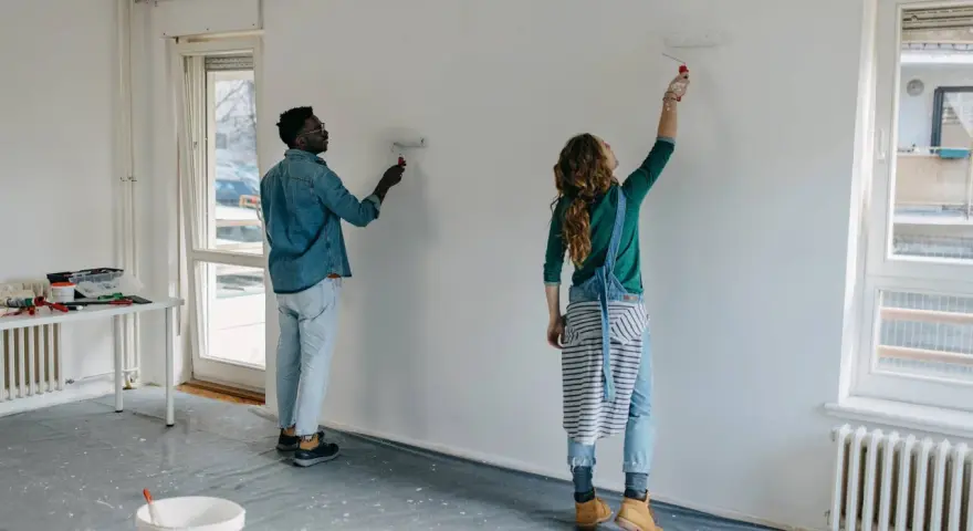 Pareja pintando una pared blanca, renovando su hogar. El hombre y la mujer usan rodillos para pintar sobre lacado, transformando el espacio.
