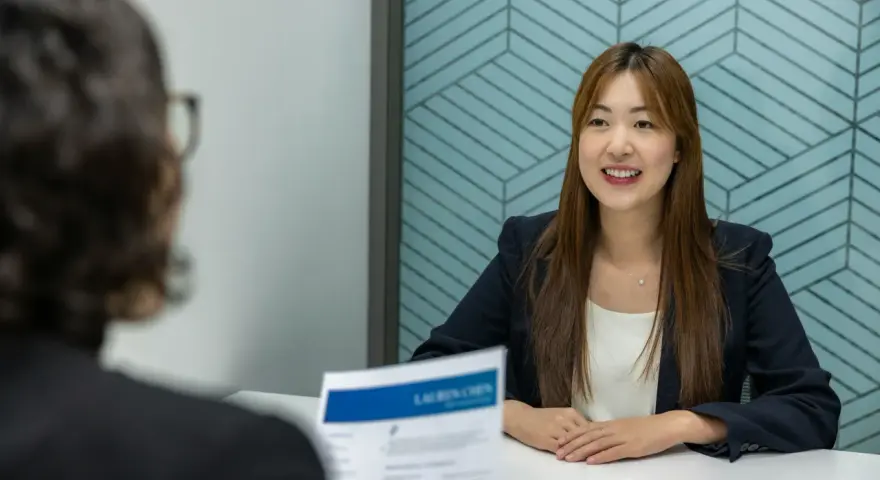 Une femme souriante en entretien, son CV sur la table. Elle semble confiante, peut-être reçoit-elle une lettre de recadrage positive pour un nouveau poste.