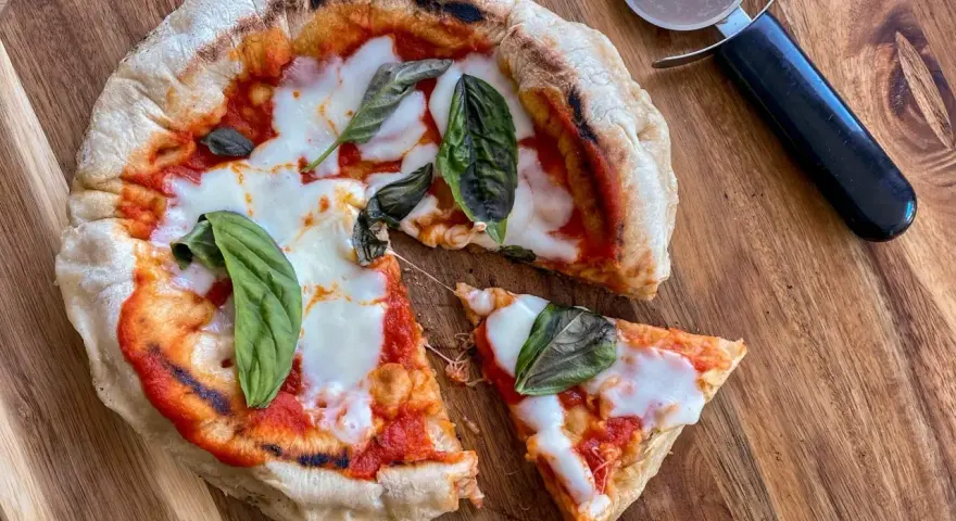 Pizza in padella appena sfornata, con pomodoro, mozzarella filante e basilico fresco, pronta per essere tagliata.