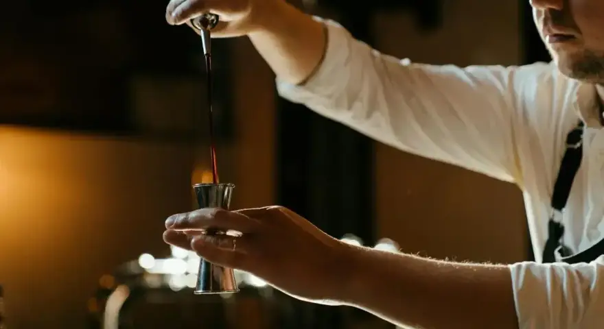 Barman nalewa ciemny płyn do jiggera, przygotowując drinka z Jägermeisterem i sokiem pomarańczowym.