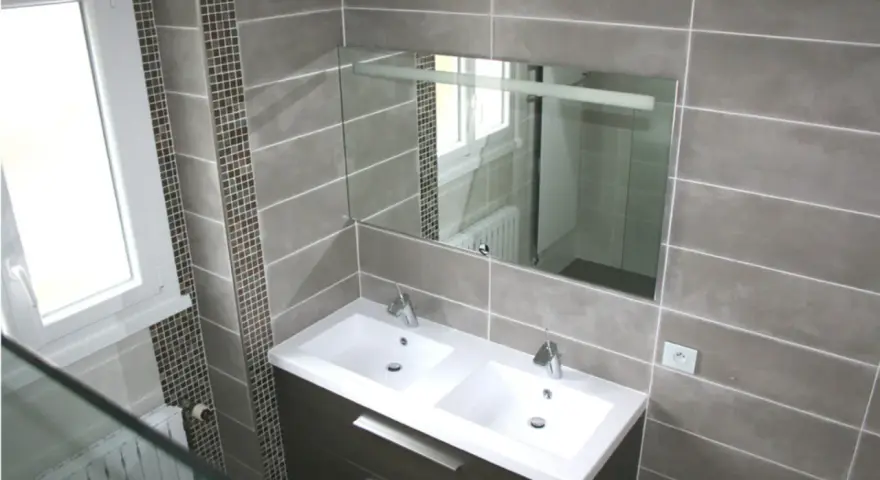 Salle de bain moderne avec double vasque. Le carrelage sol gris, posé au mur, crée une ambiance élégante.