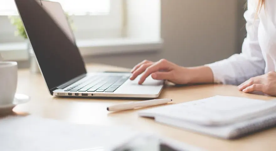 Mano su laptop, penna e quaderno. Ricerca su quanto guadagna un traduttore.